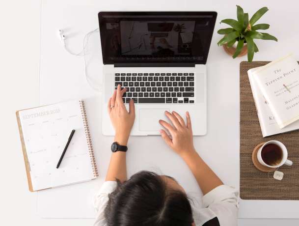 Woman typing on laptop with a notebook and tea