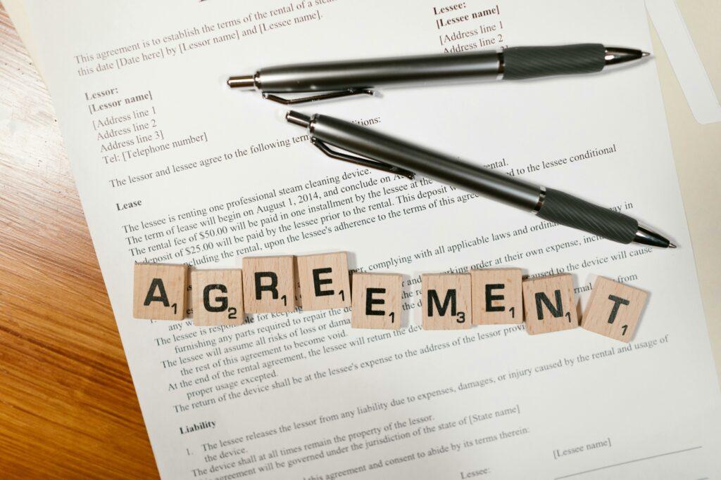 a lease agreement with two black pens and scrabble tiles spelling out the word "agreement" on top
